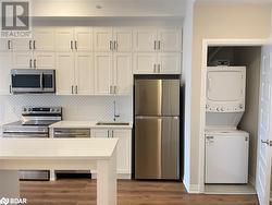 Kitchen featuring sink, backsplash, white cabinets, stacked washer and clothes dryer, and appliances with stainless steel finishes - 