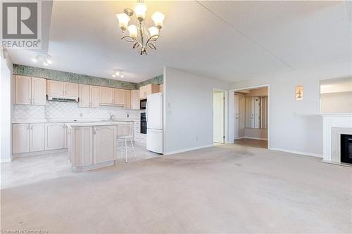 Unfurnished living room with a notable chandelier, light colored carpet, and a textured ceiling - 870 Upper Wentworth Street Unit# 202, Hamilton, ON - Indoor Photo Showing Kitchen With Fireplace