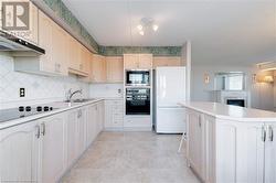 Kitchen with sink, white refrigerator, stovetop, black oven, and stainless steel microwave - 