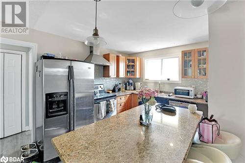 Kitchen featuring decorative backsplash, light stone counters, wall chimney range hood, and appliances with stainless steel finishes - 8876 County Road 56, Utopia, ON 