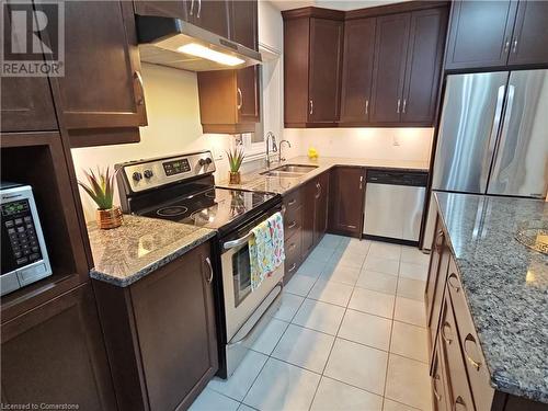 Kitchen featuring sink, light tile patterned floors, dark brown cabinets, light stone counters, and stainless steel appliances - 218 Gravel Ridge Trail, Kitchener, ON - Indoor Photo Showing Kitchen With Stainless Steel Kitchen With Double Sink