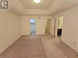 Unfurnished bedroom with light colored carpet, a raised ceiling, a walk in closet, and ensuite bath - 