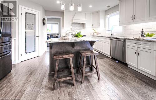 Kitchen with hanging light fixtures, light stone counters, stainless steel dishwasher, independent washer and dryer, and premium range hood - 66 Lock Street, Innerkip, ON - Indoor Photo Showing Kitchen With Upgraded Kitchen