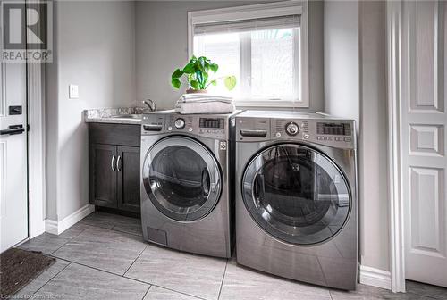 Laundry room featuring cabinets, washing machine and dryer, light tile patterned floors, and sink - 66 Lock Street, Innerkip, ON - Indoor Photo Showing Laundry Room