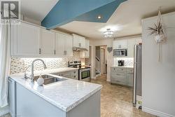 Kitchen with tasteful backsplash, white cabinets, sink, kitchen peninsula, and stainless steel appliances - 