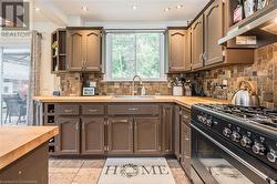 Kitchen with black range with gas cooktop, dark brown cabinetry, ventilation hood, sink, and butcher block counters - 