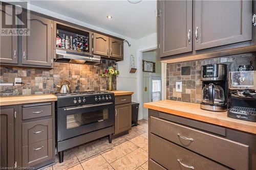 Kitchen featuring decorative backsplash, high end black range, exhaust hood, light tile patterned floors, and butcher block countertops - 48 Dane Street, Kitchener, ON - Indoor Photo Showing Kitchen