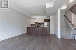 Kitchen with white cabinets, a raised ceiling, stainless steel fridge, an island with sink, and wood-type flooring - 