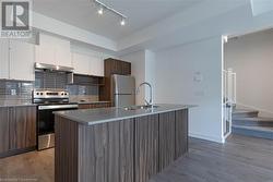 Kitchen with stainless steel appliances, a raised ceiling, light hardwood / wood-style floors, white cabinetry, and an island with sink - 