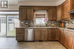 Kitchen with sink, decorative backsplash, light tile patterned floors, appliances with stainless steel finishes, and light stone counters - 