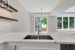 Kitchen with decorative backsplash, light stone counters, white cabinets, and pendant lighting - 