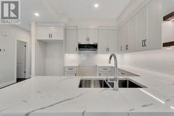 Kitchen featuring backsplash, light stone countertops, sink, and white cabinets - 