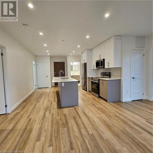 Kitchen with a center island with sink, white cabinets, sink, light hardwood / wood-style floors, and range - 525 New Dundee Road Unit# 602, Kitchener, ON - Indoor Photo Showing Kitchen