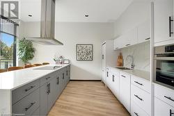 Kitchen featuring gray cabinetry, extractor fan, sink, white cabinets, and oven - 