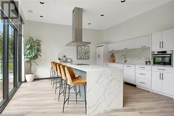 Kitchen with backsplash, island range hood, a kitchen island, white cabinetry, and oven - 