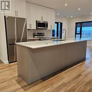 Kitchen with stove, a center island with sink, sink, light wood-type flooring, and fridge - 