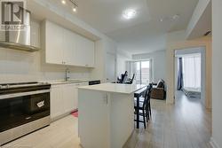 Kitchen featuring a center island, sink, wall chimney range hood, stainless steel range oven, and white cabinets - 