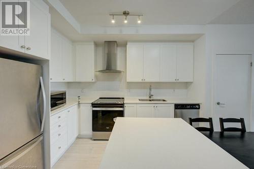 Kitchen with wall chimney exhaust hood, white cabinetry, sink, and appliances with stainless steel finishes - 55 Duke Street Unit# 322, Kitchener, ON - Indoor Photo Showing Kitchen With Double Sink