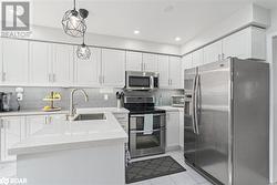 Kitchen featuring appliances with stainless steel finishes, decorative light fixtures, white cabinetry, and sink - 