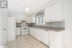 Kitchen with ceiling fan, sink, light tile patterned flooring, white appliances, and white cabinets - 