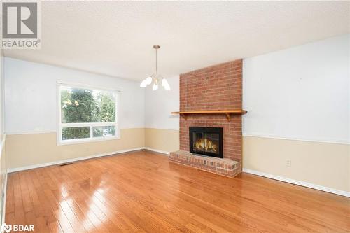 Unfurnished living room with hardwood / wood-style floors, a textured ceiling, a brick fireplace, and a notable chandelier - 15 Oakington Place, Mississauga, ON - Indoor Photo Showing Living Room With Fireplace