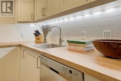 Kitchen featuring wooden counters, tasteful backsplash, sink, cream cabinetry, and dishwasher - 