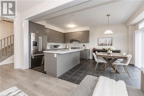 Kitchen featuring stainless steel refrigerator with ice dispenser, gray cabinetry, dark wood-type flooring, a center island with sink, and decorative light fixtures - 116 Whithorn Crescent, Caledonia, ON - Indoor