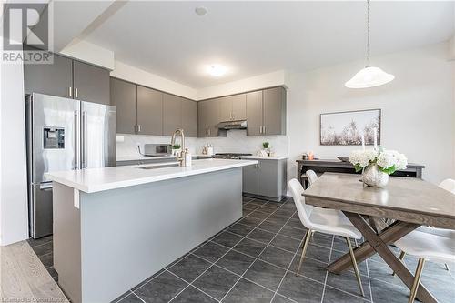 Kitchen featuring decorative backsplash, stainless steel refrigerator with ice dispenser, gray cabinetry, a kitchen island with sink, and decorative light fixtures - 116 Whithorn Crescent, Caledonia, ON - Indoor