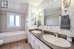 Bathroom with tile patterned flooring, a relaxing tiled tub, crown molding, toilet, and vanity - 