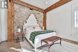 Bedroom featuring beam ceiling, a barn door, and light hardwood / wood-style floors - 