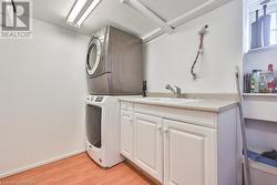 Washroom featuring cabinets, sink, stacked washer / dryer, and light hardwood / wood-style flooring - 