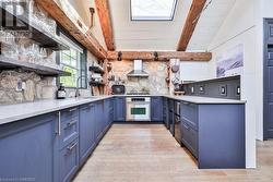 Kitchen featuring appliances with stainless steel finishes, wall chimney exhaust hood, sink, blue cabinetry, and vaulted ceiling with beams - 