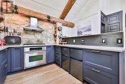 Kitchen with wall chimney range hood, light hardwood / wood-style flooring, vaulted ceiling with beams, blue cabinetry, and appliances with stainless steel finishes - 