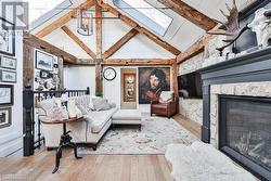 Living room featuring vaulted ceiling with beams, a stone fireplace, light wood-type flooring, and a chandelier - 