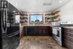 Kitchen offers ample cabinetry and shelving to match the home's interior. Large window overlooks driveway. - 