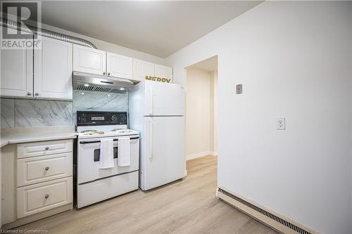 Kitchen with white cabinetry, baseboard heating, tasteful backsplash, light hardwood / wood-style flooring, and white appliances - 212 Westcourt Place, Waterloo, ON - Indoor Photo Showing Kitchen