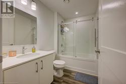 Full bathroom with toilet, vanity, combined bath / shower with glass door, and hardwood / wood-style floors - 