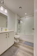 Full bathroom with toilet, vanity, bath / shower combo with glass door, and hardwood / wood-style flooring - 