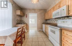 Kitchen featuring white appliances, light tile patterned floors, tasteful backsplash, and light brown cabinets - 