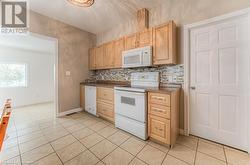 Kitchen featuring tasteful backsplash, light tile patterned floors, light brown cabinetry, and white appliances - 