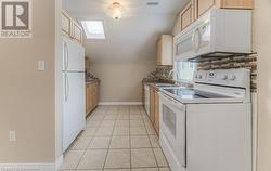 Kitchen featuring light tile patterned flooring, sink, light brown cabinets, and white appliances - 