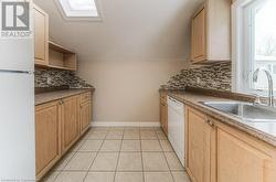 Kitchen with light tile patterned floors, backsplash, light brown cabinets, white appliances, and sink - 