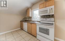 Kitchen with decorative backsplash, white appliances, light tile patterned flooring, lofted ceiling, and sink - 