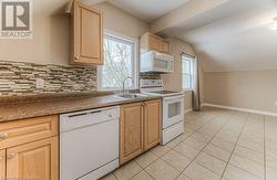 Kitchen featuring lofted ceiling, sink, white appliances, light brown cabinets, and light tile patterned floors - 