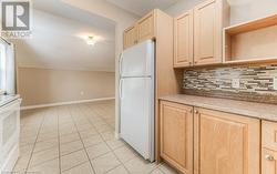 Kitchen with white fridge, decorative backsplash, light tile patterned floors, light brown cabinetry, and range - 