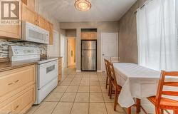 Kitchen with tile countertops, decorative backsplash, white appliances, light brown cabinets, and light tile patterned floors - 