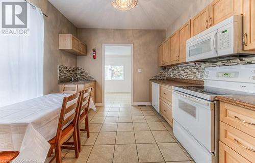 Kitchen with light tile patterned floors, light brown cabinets, tasteful backsplash, and white appliances - 67 Wellington Street N, Kitchener, ON - Indoor Photo Showing Kitchen