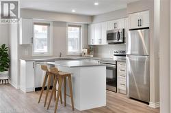 Kitchen featuring a kitchen island, a breakfast bar, white cabinets, stainless steel appliances, and light wood-type flooring - 