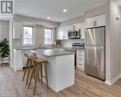 Kitchen with stainless steel appliances, a center island, light hardwood / wood-style floors, white cabinets, and a kitchen bar - 