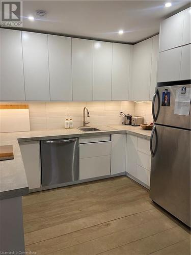 Kitchen featuring white cabinetry, light wood-type flooring, dishwashing machine, and refrigerator - 67 Louisa Street, Kitchener, ON - Indoor Photo Showing Kitchen With Upgraded Kitchen